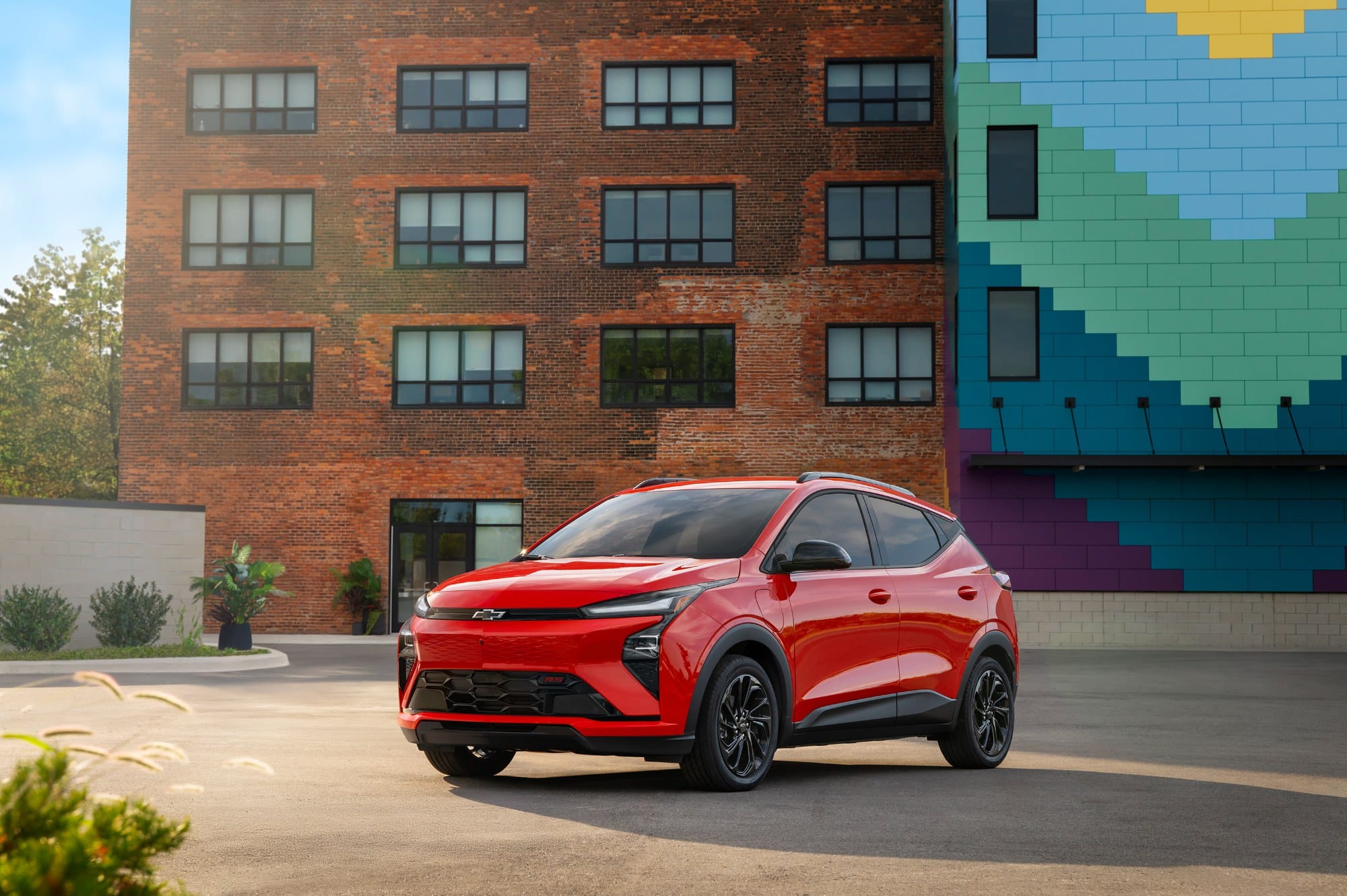 2027 Chevrolet Bolt RS in red, front three quarter view, parked outside a brick building