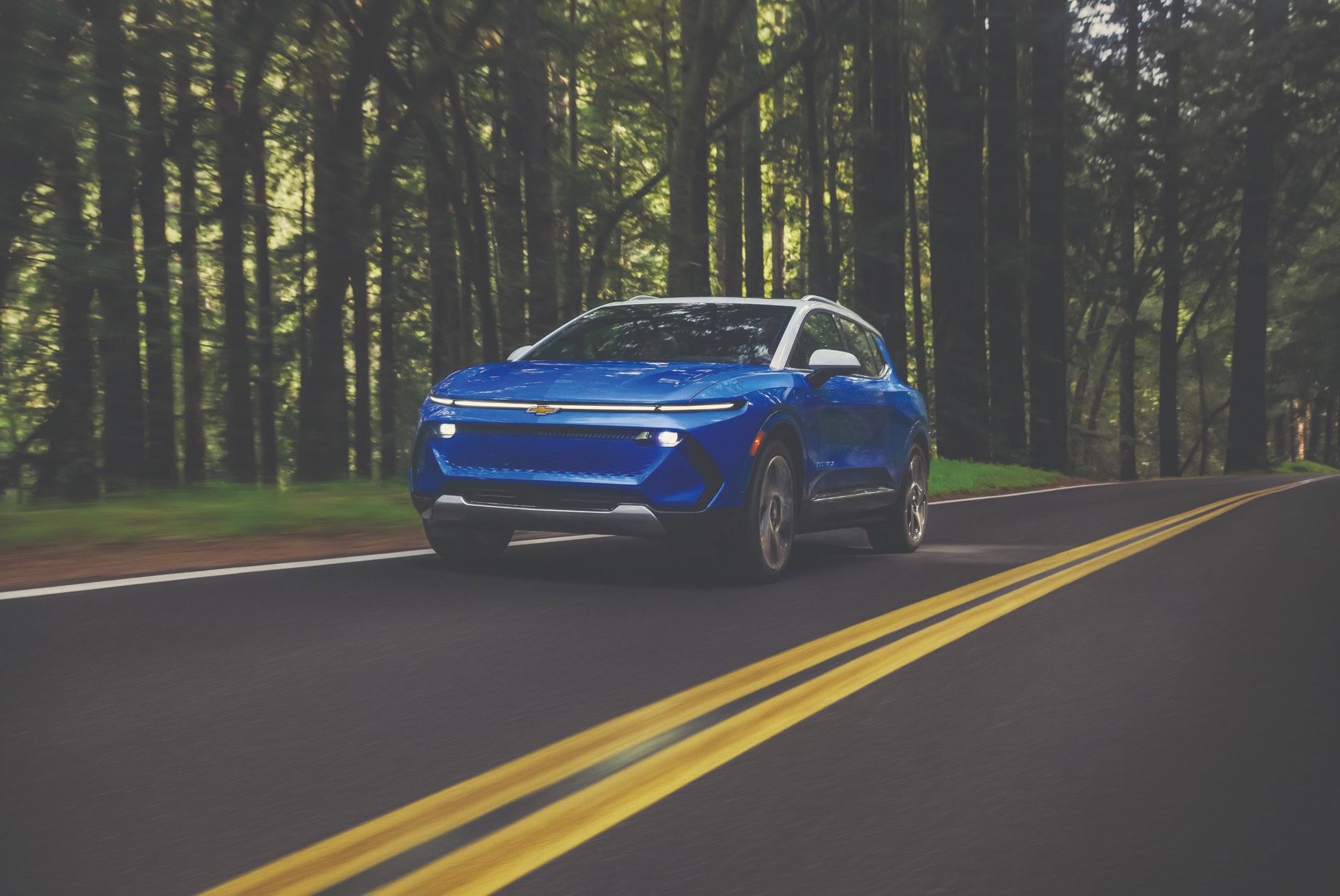 2027 Chevrolet Equinox EV in Riptide Blue Metallic driving on a forest road
