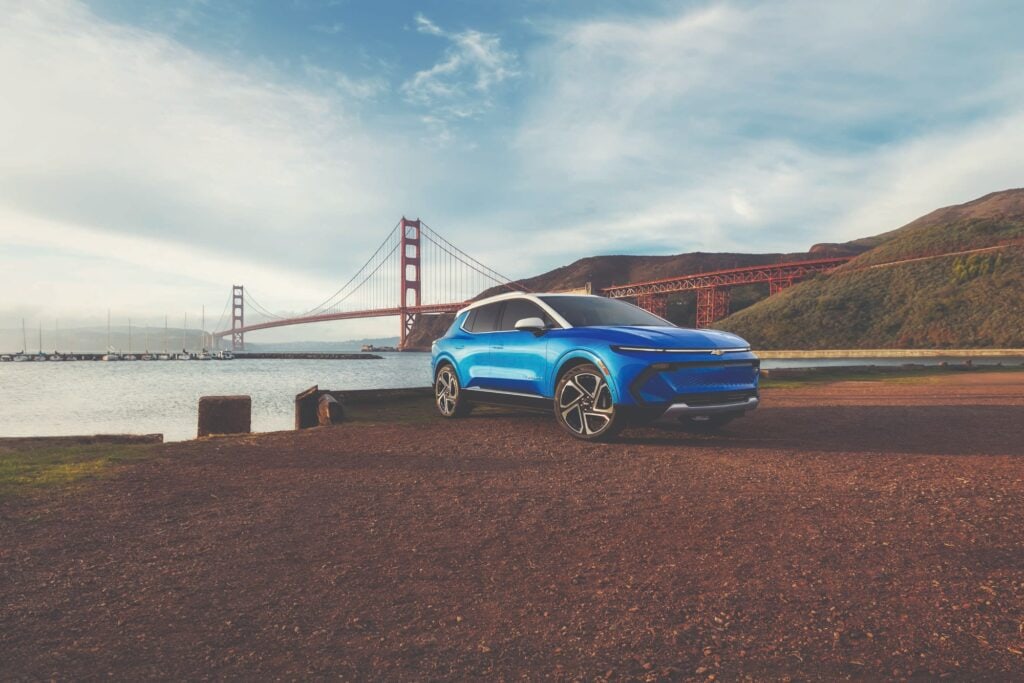 2027 Chevrolet Equinox EV in Riptide Blue Metallic, front three quarter view, parked in front of a bridge