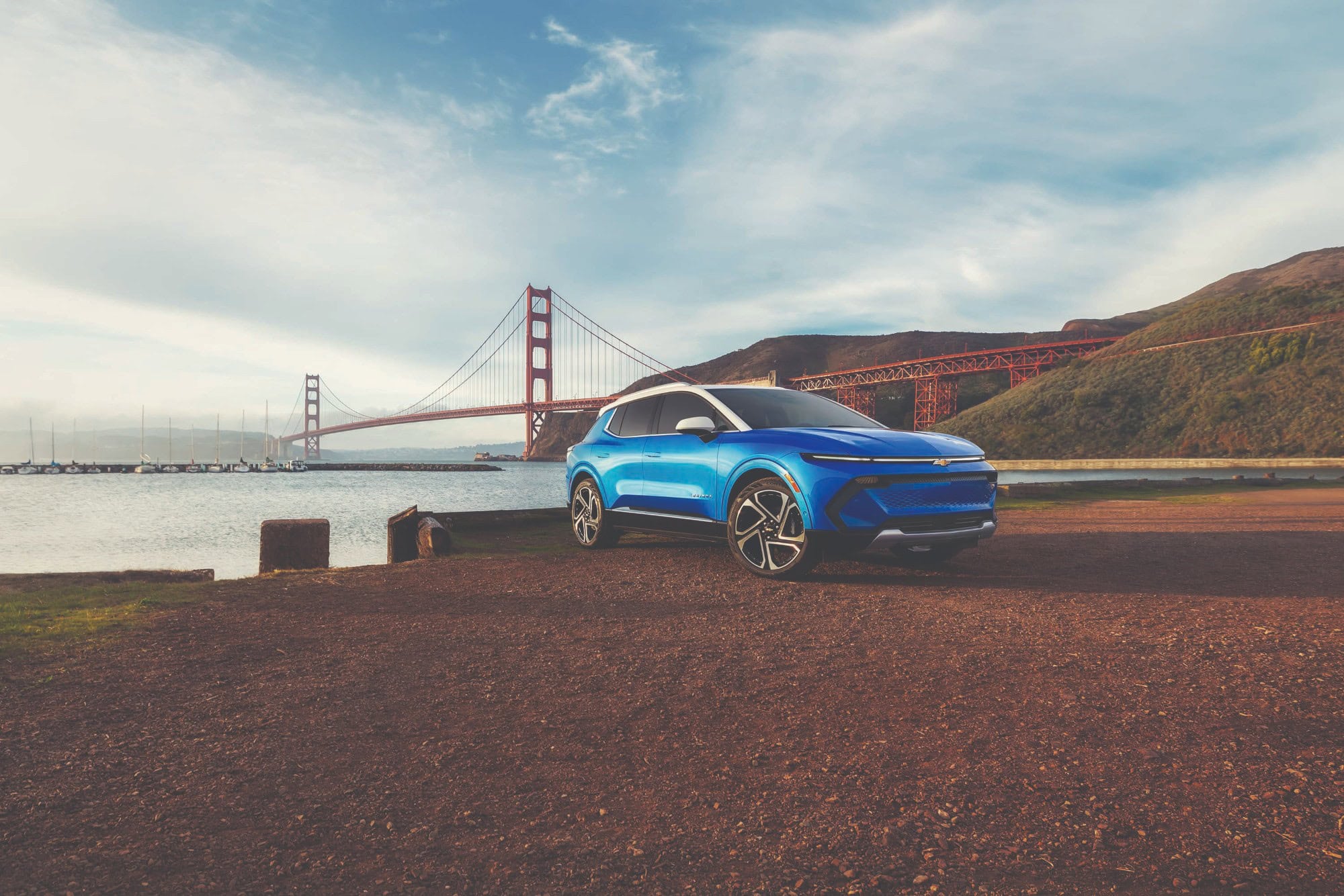2027 Chevrolet Equinox EV in Riptide Blue Metallic, front three quarter view, parked in front of a bridge