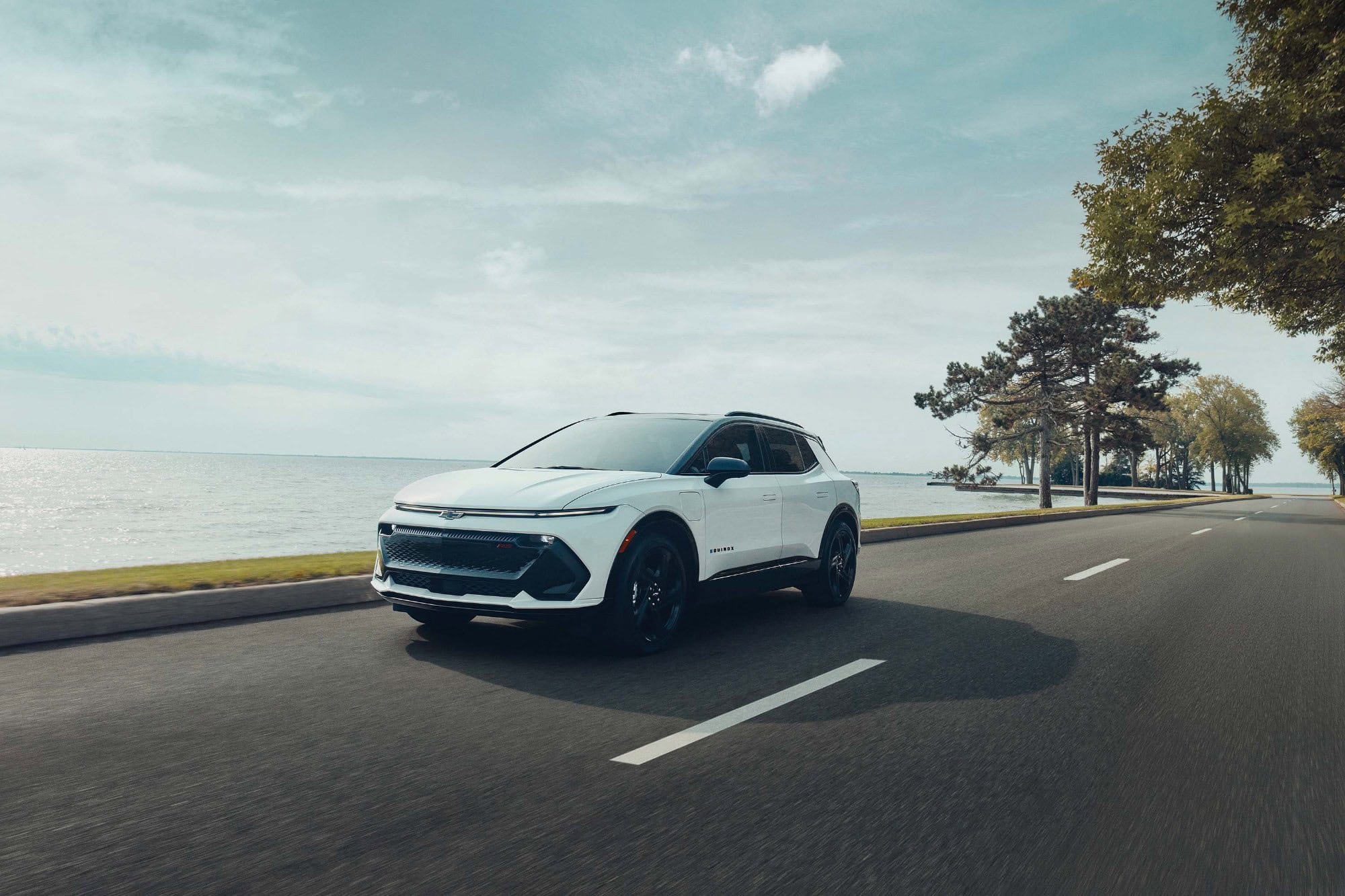 2027 Chevrolet Equinox EV RS in Polar White Tricoat driving on a scenic road