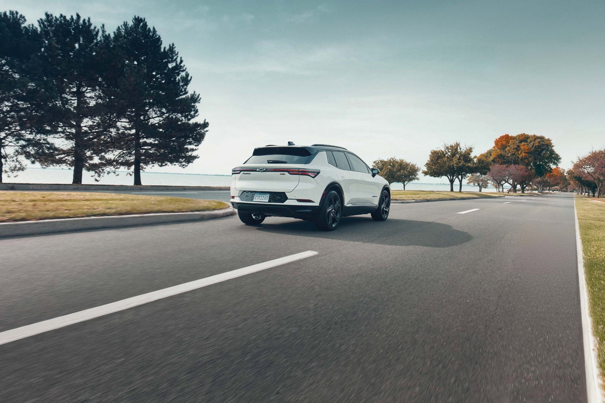 2027 Chevrolet Equinox EV RS in Polar White Tricoat, rear three quarter view, driving on a scenic road