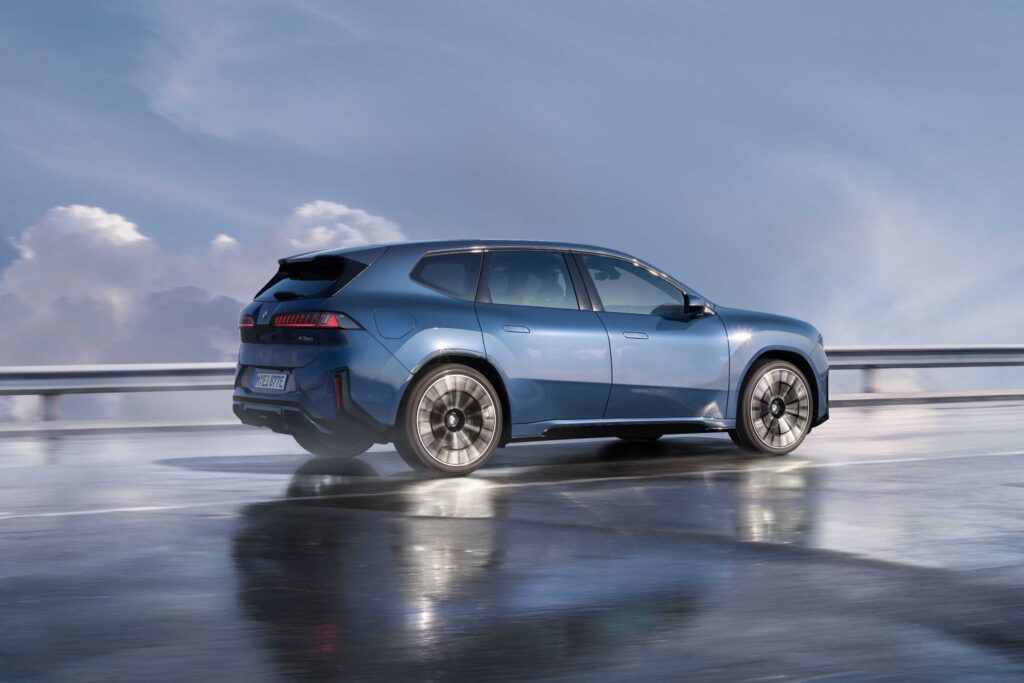 BMW iX3 50 xDrive in blue, rear three quarter view on a wet road, European model shown