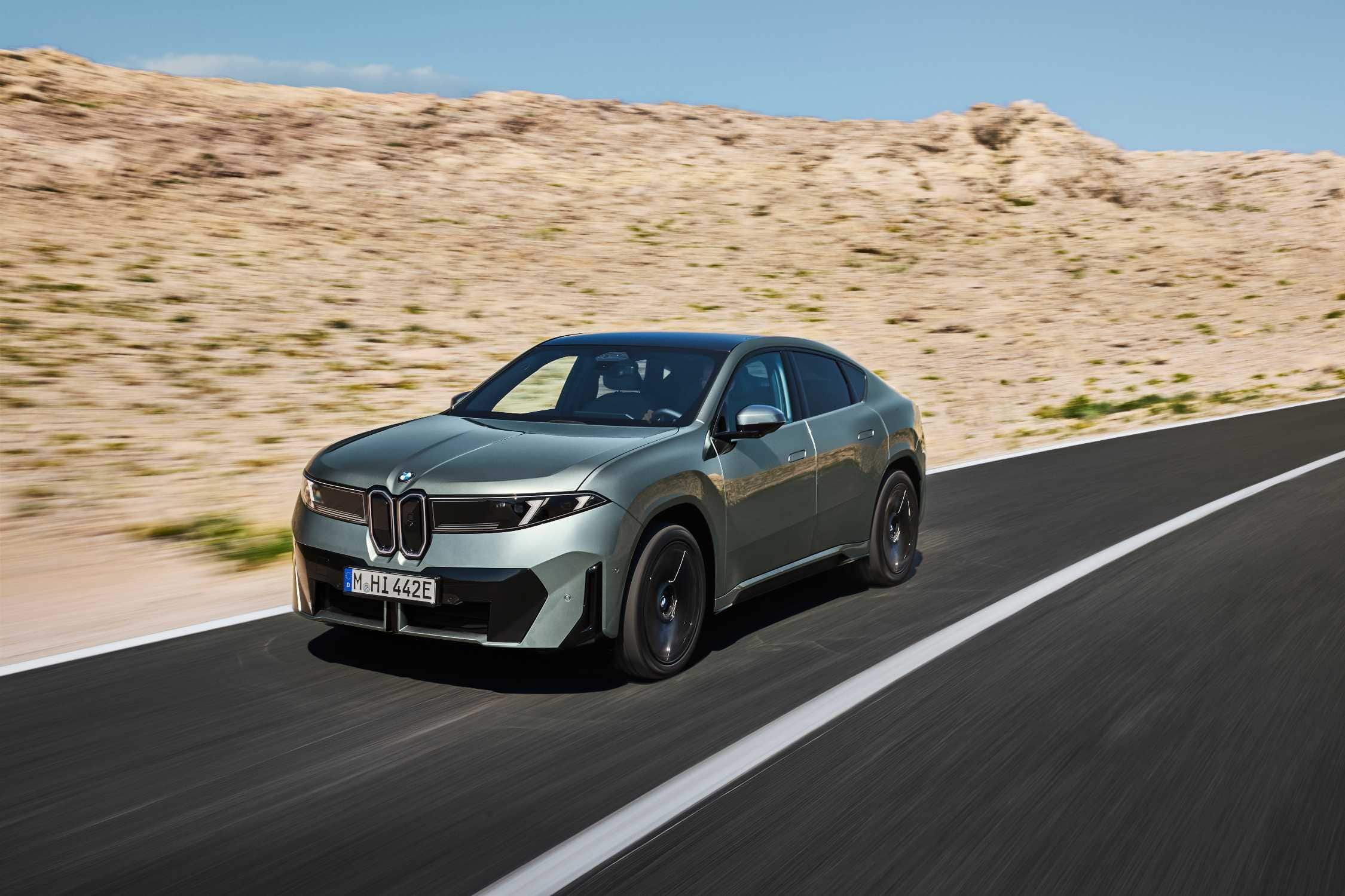 BMW iX4 in green, front three quarter view on a road